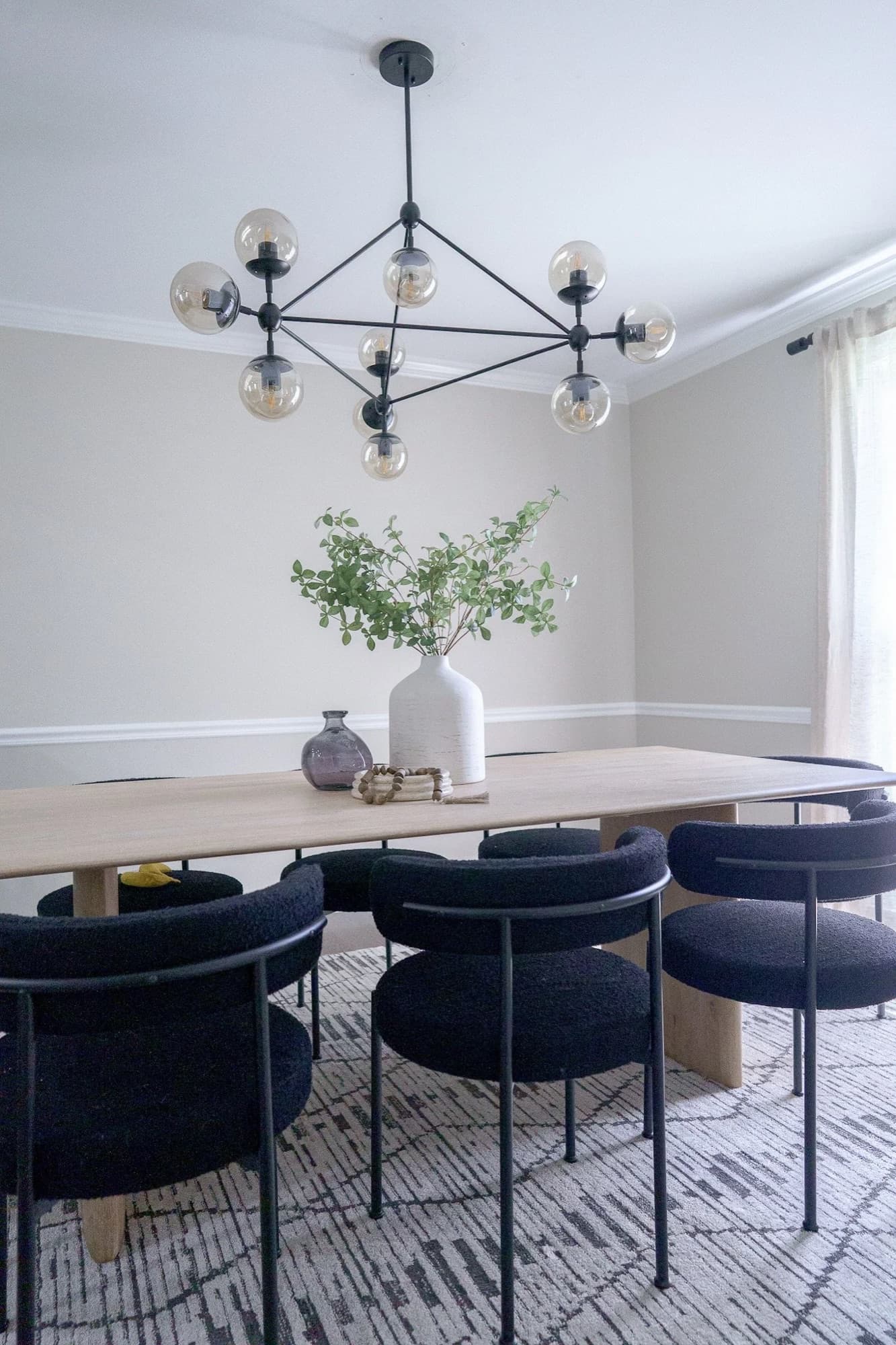 Dining room with a light-wood table, navy boucle chairs, and a black orb chandelier.
