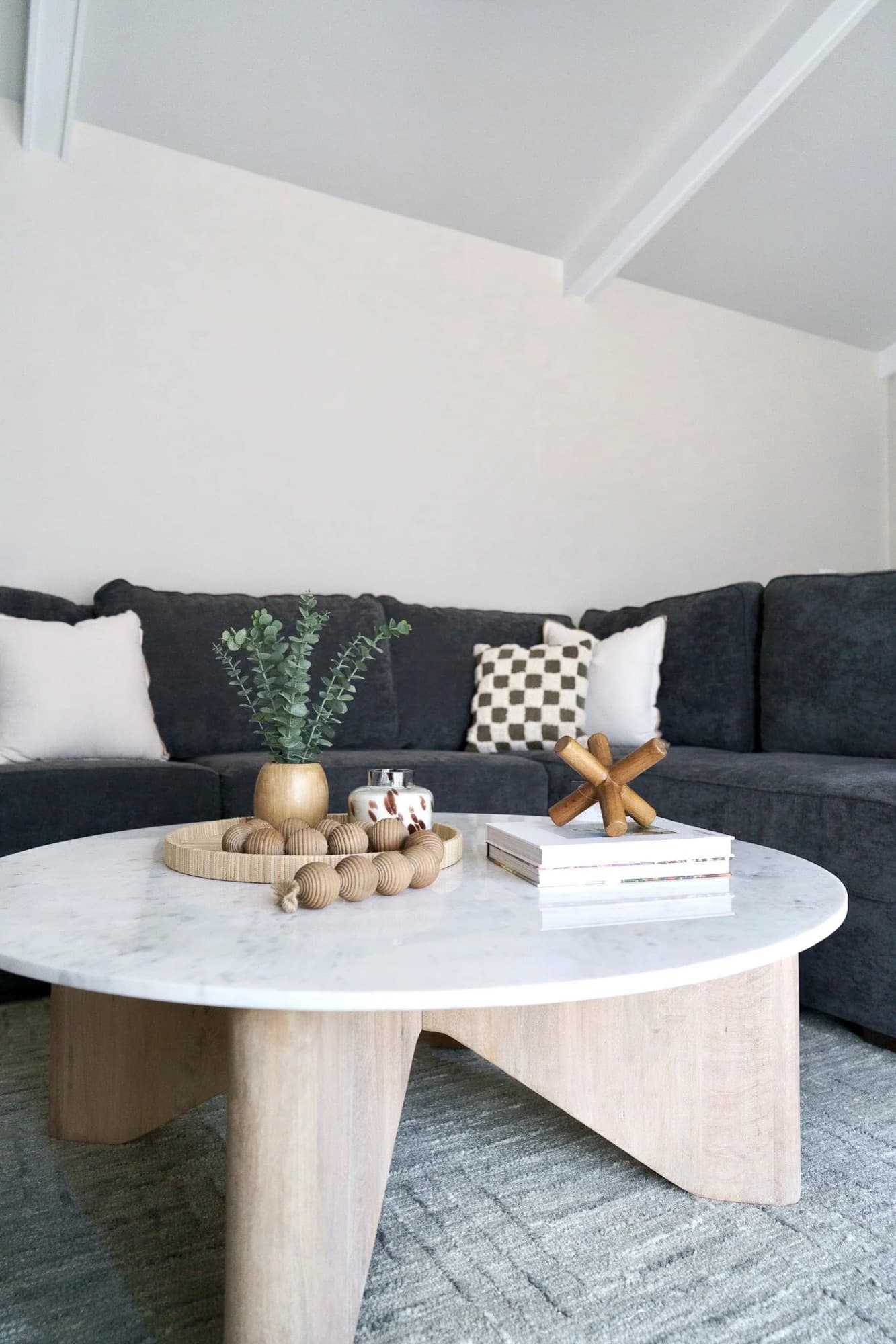 Living room detail: a round marble coffee table with a sculptural wood base styled with books and greenery in front of a charcoal sectional.