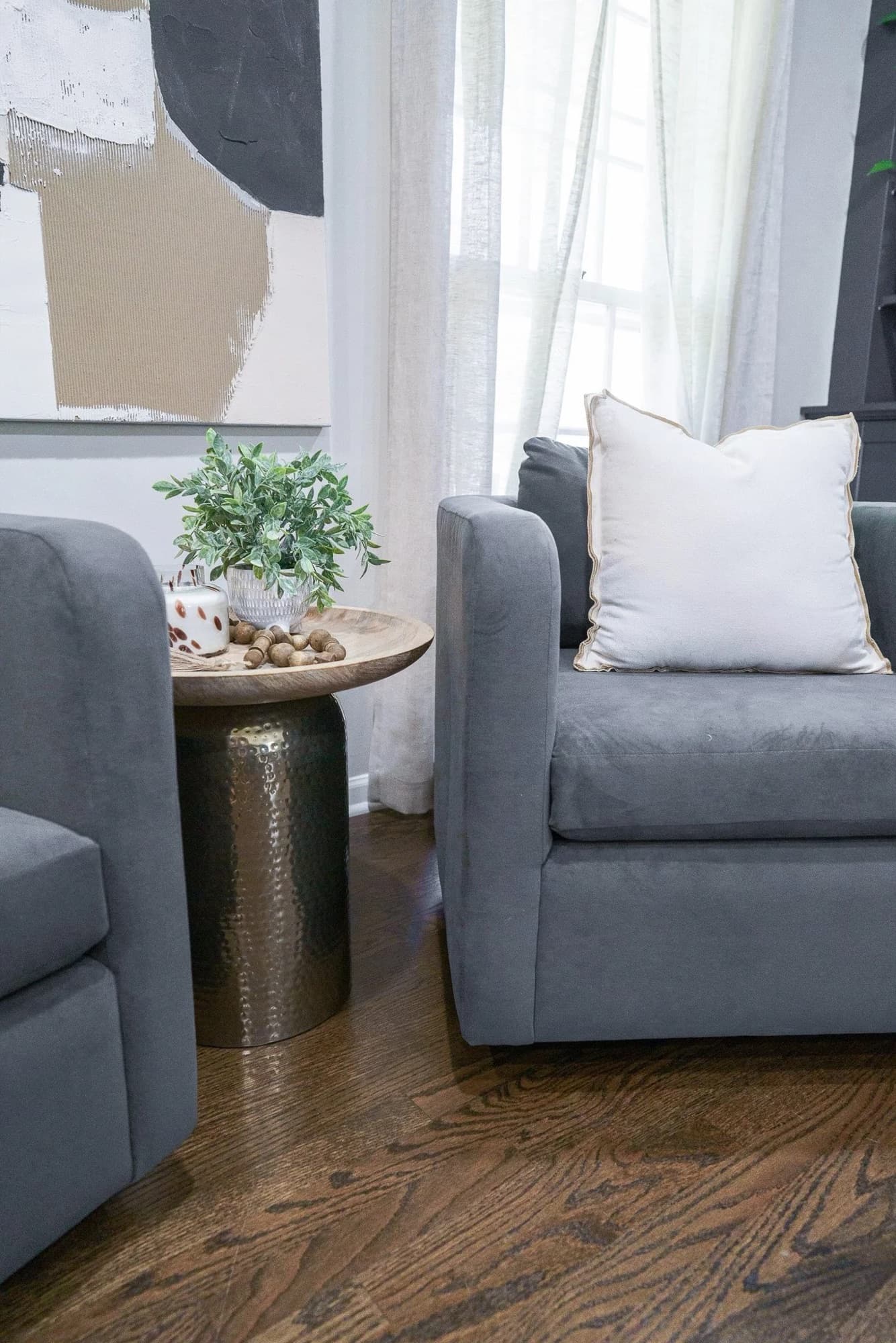 Sitting area with two gray armchairs flanking a hammered-brass drum table and layered abstract art.