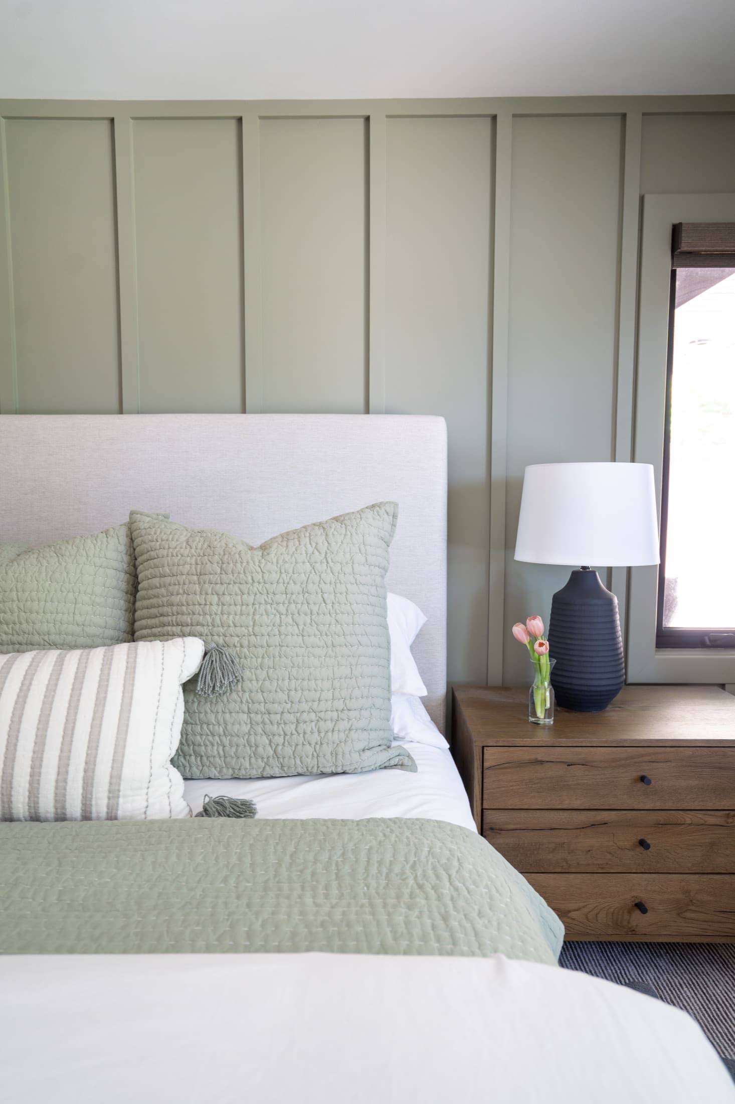 Close-up of peach tulips on the marble island beneath a black barn-style pendant and wood plank ceiling.