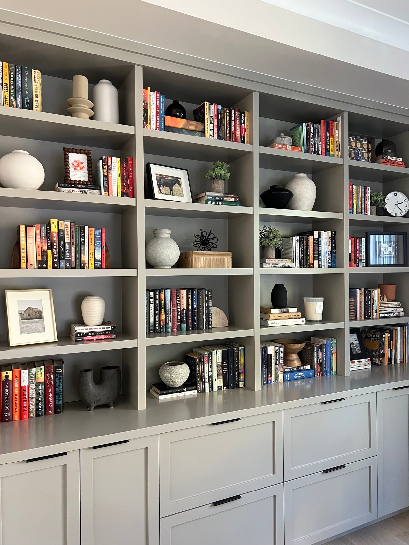 Floor-to-ceiling taupe built-in shelving styled with books, ceramics, and framed art above cabinet storage.