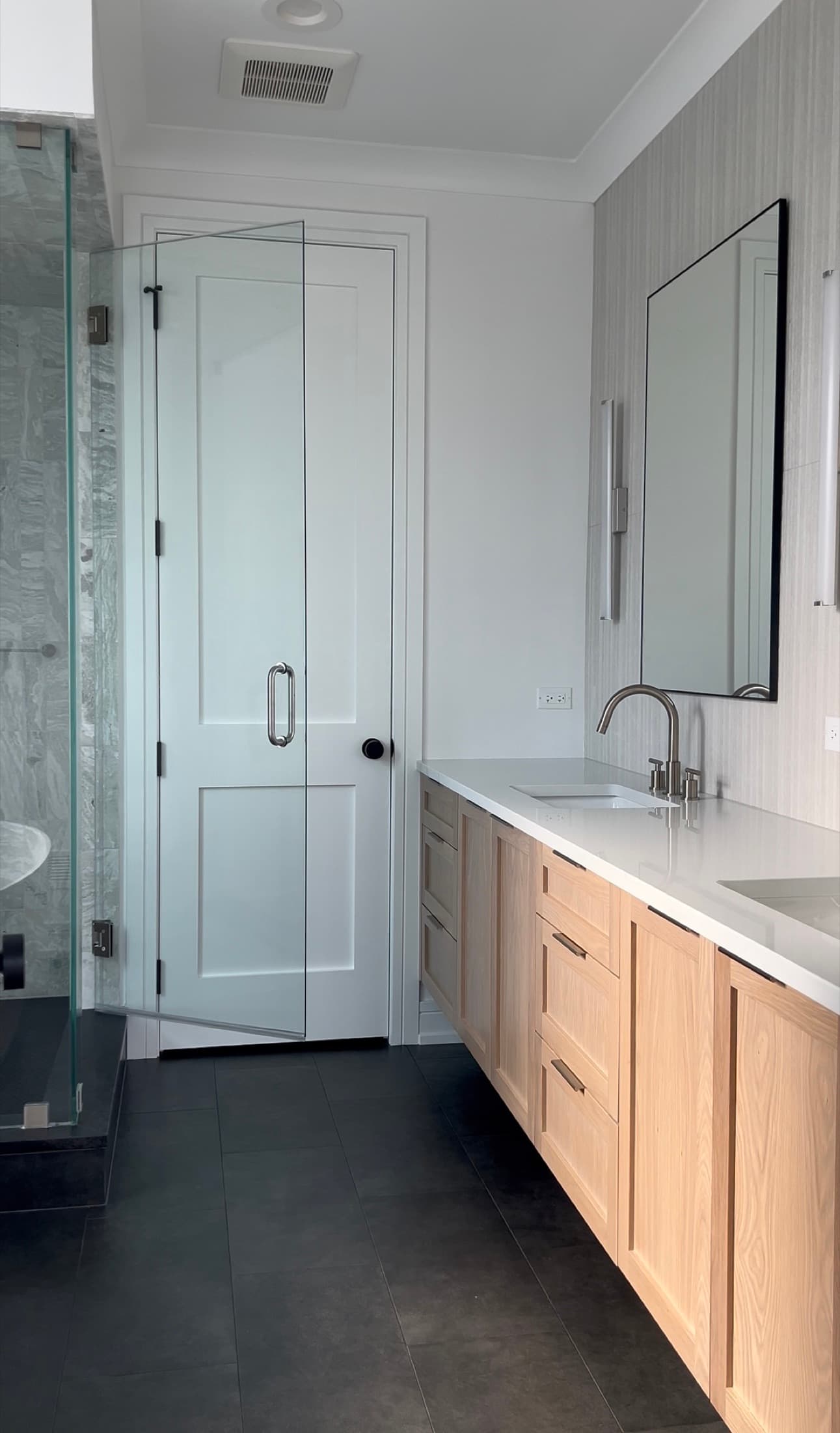Primary bathroom with a white-oak double vanity, quartz counter, black-framed mirror, and a glass walk-in shower.